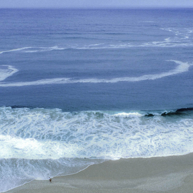 Blick von oben auf Meer, Brandung und einen einzelnen Menschen am Strand