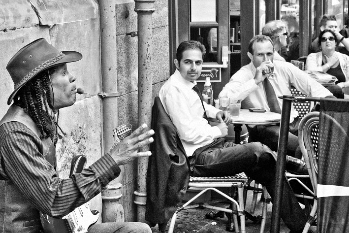 Straßenmusiker vor einem Café mit aufmerksamen Gästen